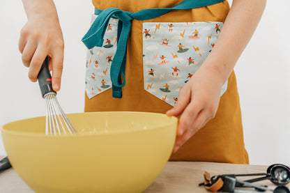 Kids surf apron Durable child apron Soft fabric apron Leather accent apron Bronze details apron Surf-themed apron Child kitchen apron Beach style apron Eco-friendly kids apron Stylish children's apron Durable apron for kids Kids cooking apron Leather strap apron Ocean design apron