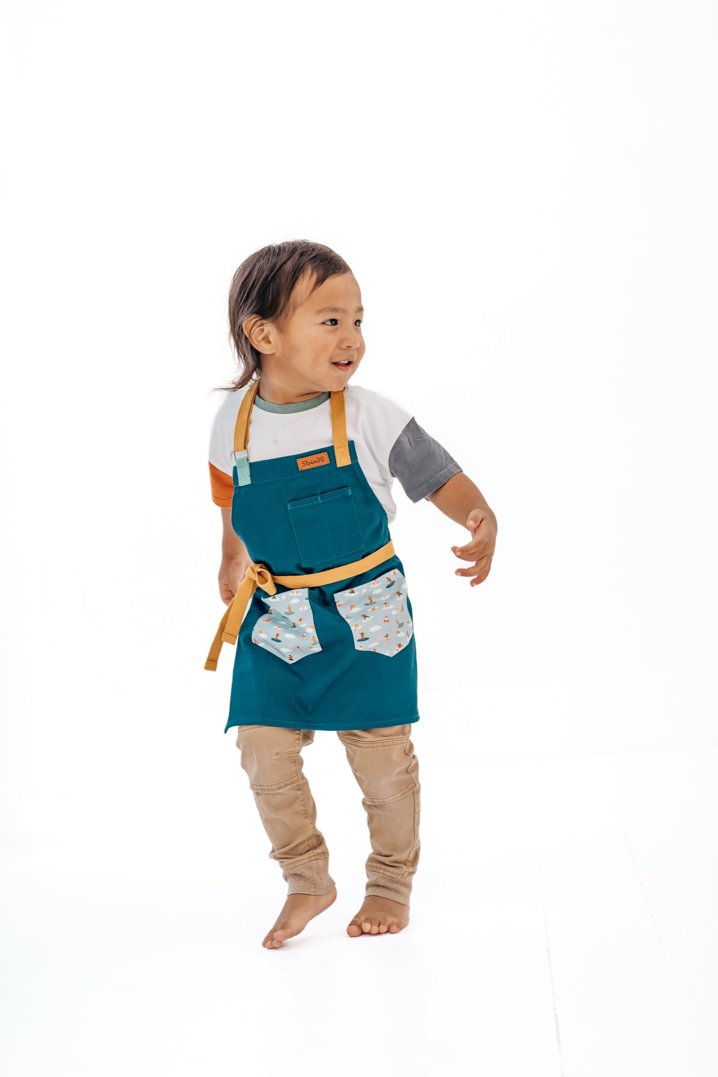 Sturdy children's cooking apron Kids surf apron Durable child apron Soft fabric apron Leather accent apron Bronze details apron Surf-themed apron Child kitchen apron Beach style apron Eco-friendly kids apron Stylish children's apron Durable apron for kids Kids cooking apron Leather strap apron Ocean design apron