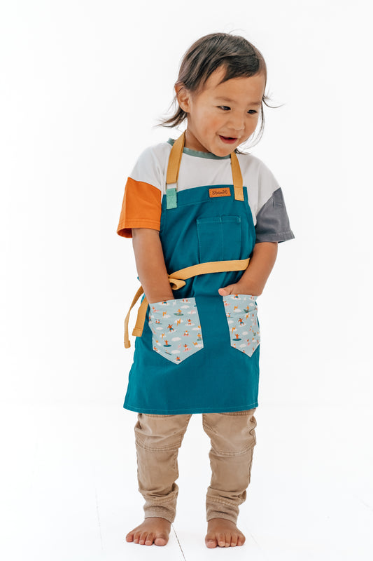 Sturdy children's cooking apron Kids surf apron Durable child apron Soft fabric apron Leather accent apron Bronze details apron Surf-themed apron Child kitchen apron Beach style apron Eco-friendly kids apron Stylish children's apron Durable apron for kids Kids cooking apron Leather strap apron Ocean design apron