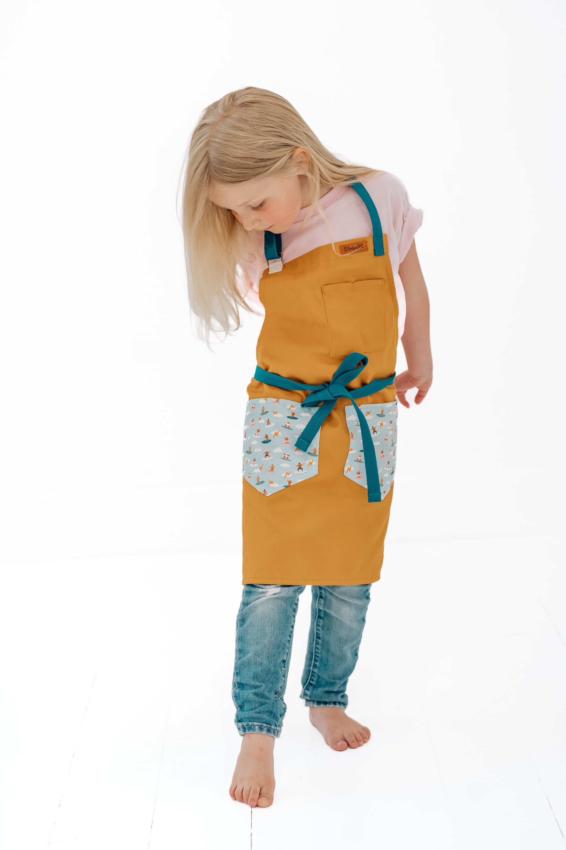 Kids surf apron Durable child apron Soft fabric apron Leather accent apron Bronze details apron Surf-themed apron Child kitchen apron Beach style apron Eco-friendly kids apron Stylish children's apron Durable apron for kids Kids cooking apron Leather strap apron Ocean design apron