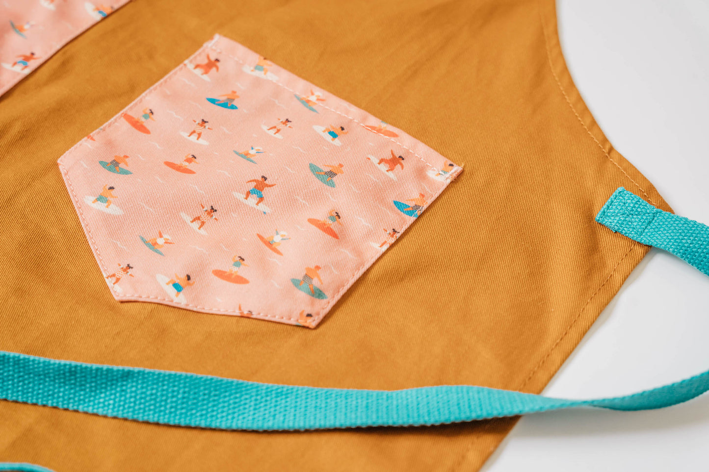 Child surf design apron Durable kids apron Soft fabric child apron Kids apron with leather accents Bronze detailed child apron Surf-themed children's apron Kids kitchen apron durable Leather strap kids apron Ocean design child apron Sturdy kids cooking apron Child apron with bronze accents High-quality kids apron Beach style children’s apron Kid-friendly surf apron