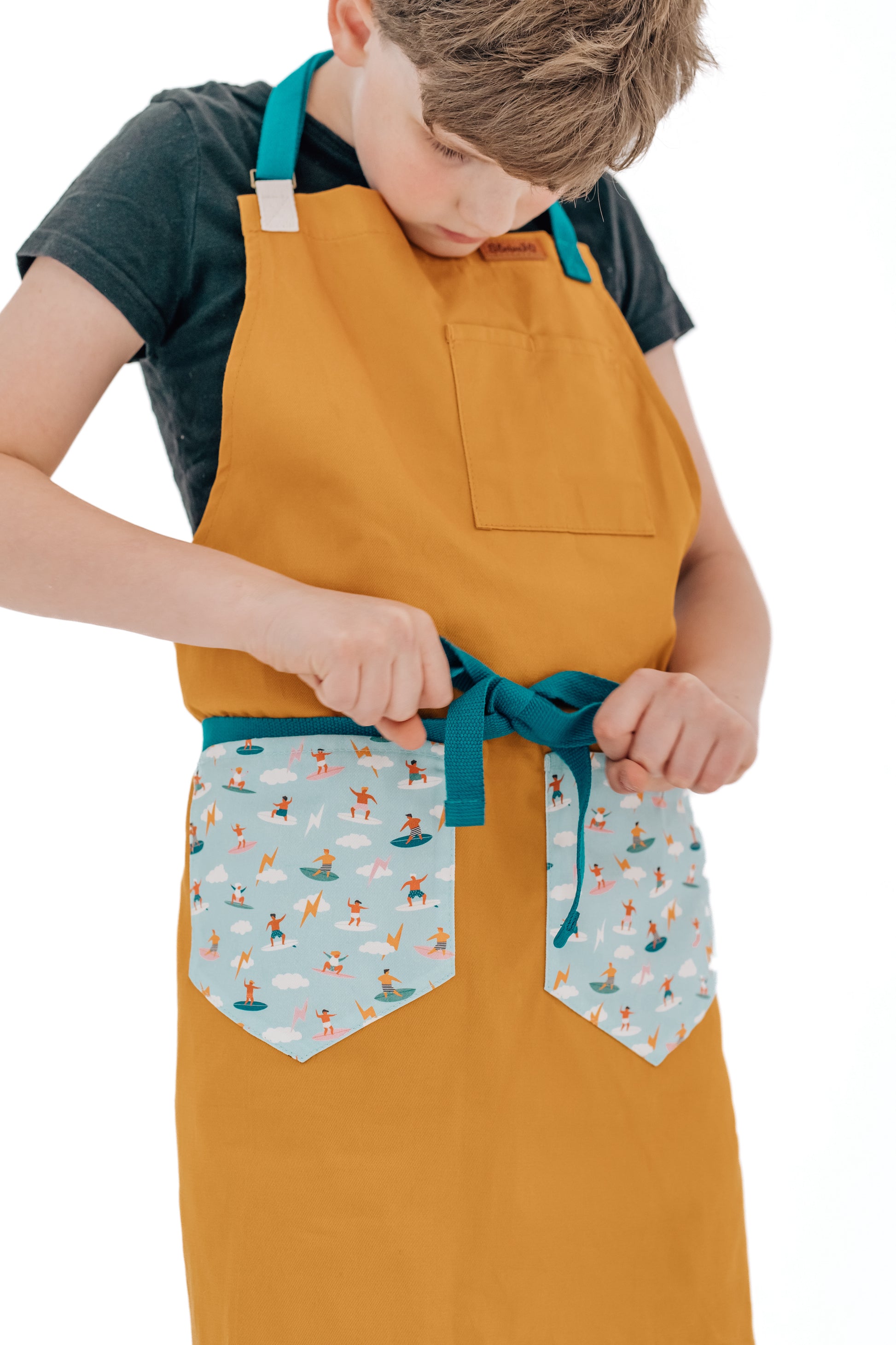 Kids surf apron Durable child apron Soft fabric apron Leather accent apron Bronze details apron Surf-themed apron Child kitchen apron Beach style apron Eco-friendly kids apron Stylish children's apron Durable apron for kids Kids cooking apron Leather strap apron Ocean design apron